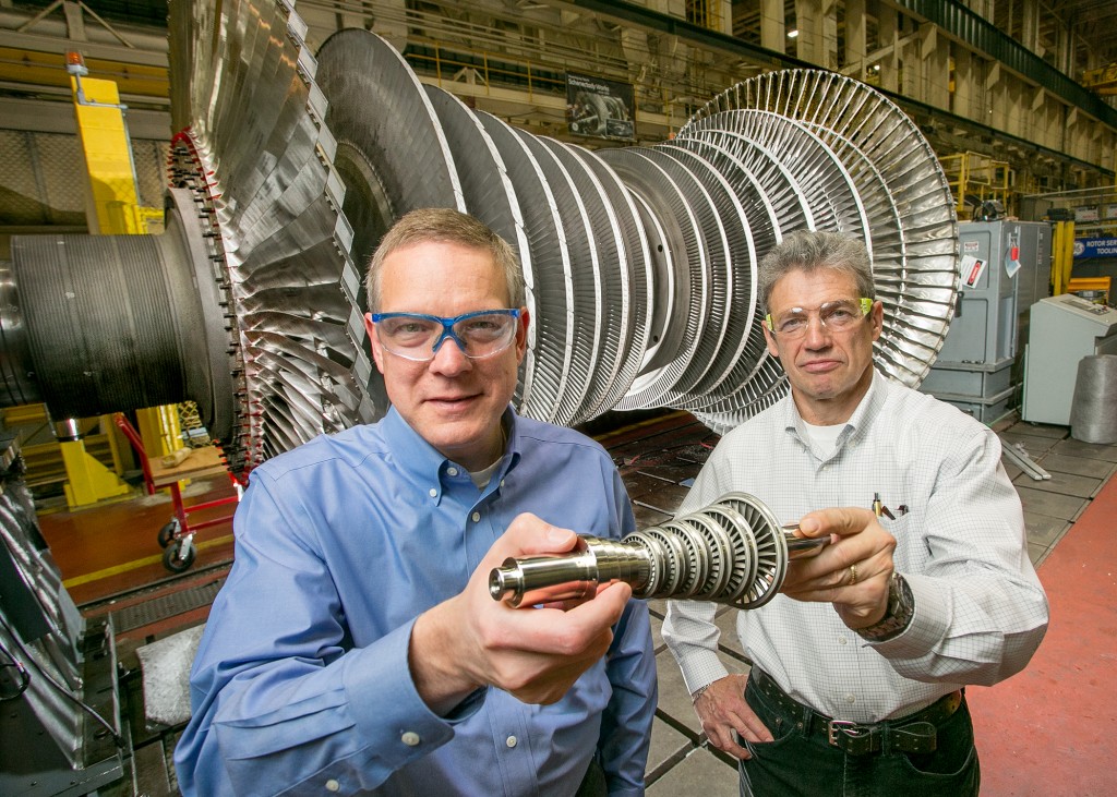 GE engineers pose in front of a full-scale turbine with a 3D printed miniature version. Courtesy of GE Global Research.