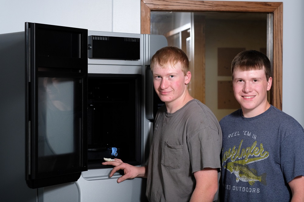Ryan and his brother stand in front of the AM system used to build his prosthetic. Courtesy of Chad Greene.