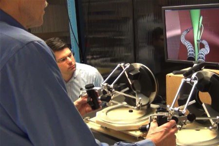 Fig. 7. While simulation software dramatically sped up product design, it also provided a side benefit as a training tool for the surgeon. At left, Fowler tests the performance of the master controllers linked to feedback from a simulation of the robotic arms in action, as a Ximedica engineer looks on.